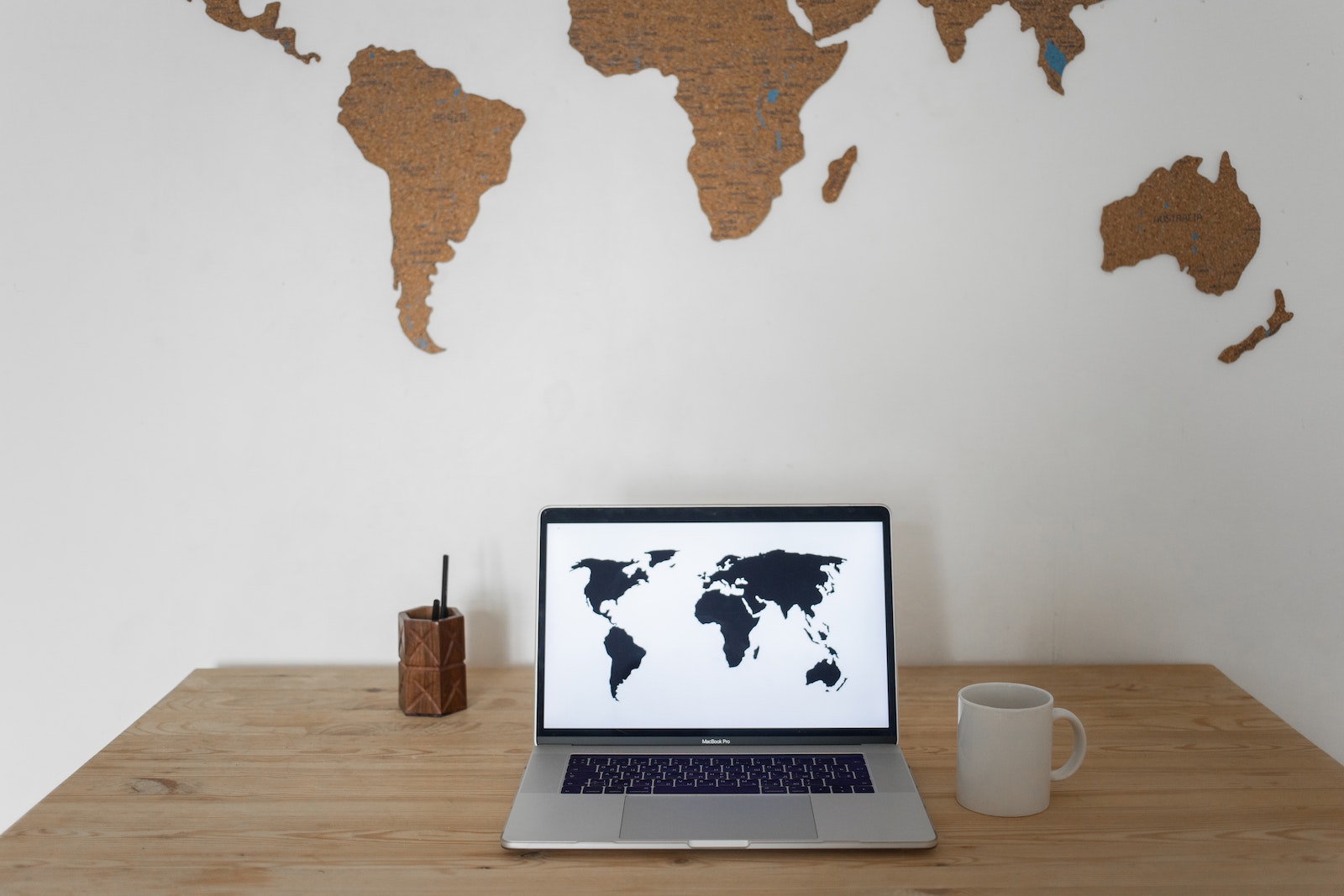 Black world map on laptop screen and ceramic cup with pen container placed on table against silhouettes of continents